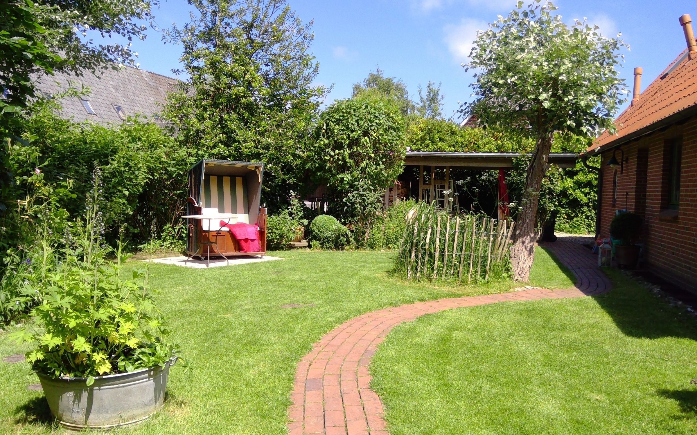 Eingezäunter, blühender Garten mit Strandkorb am Ferienhaus.